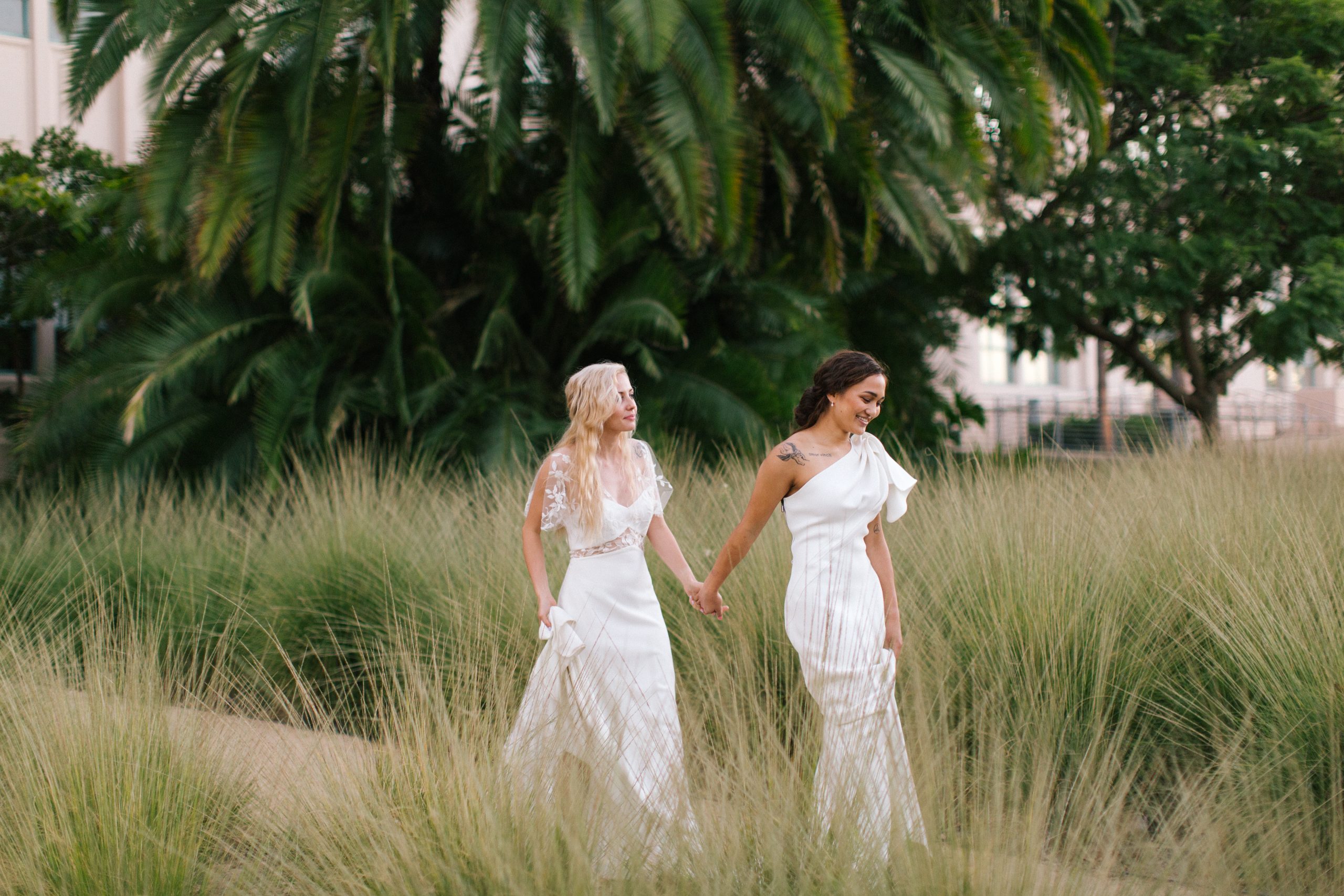 two brides walking hand in hand through greenery